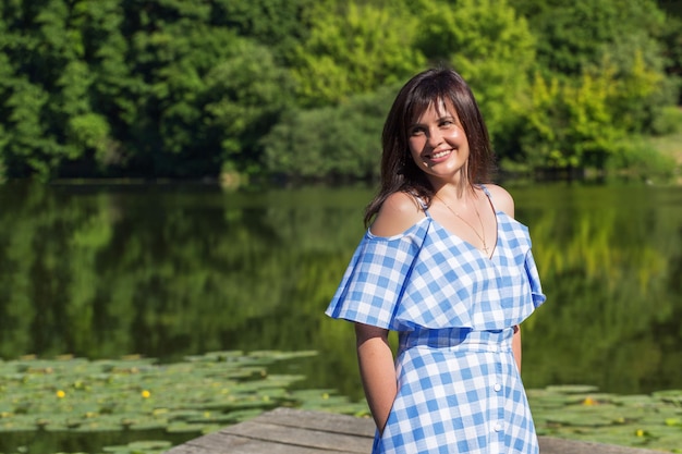 Portret van een jonge vrouw met donker haar wiens staat van een bos en meer op een zonnige zomerdag