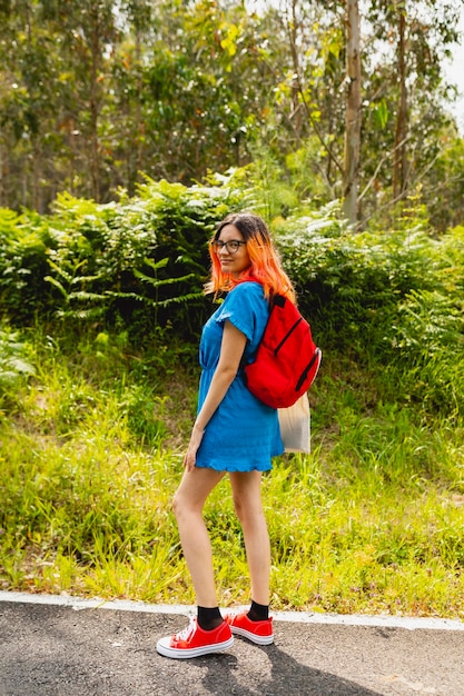 Portret van een jonge vrouw met een blauwe jurk sneakers en een rode rugzak tijdens een wandeling door een landelijk gebied in Galicië