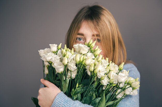 Portret van een jonge vrouw met een boeket rozen op een grijze achtergrond