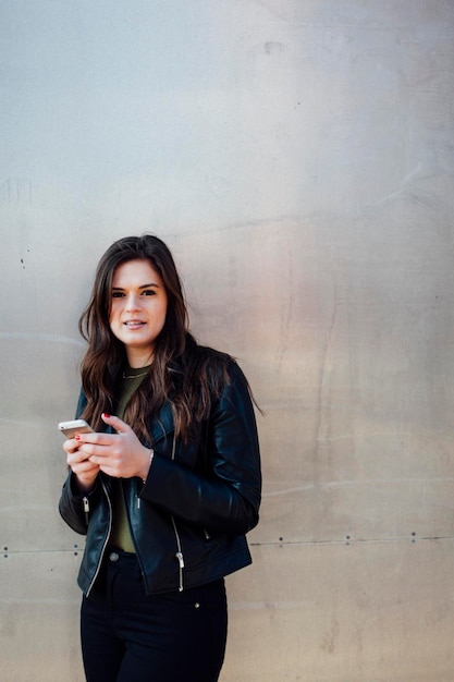 Portret van een jonge vrouw met een mobiele telefoon tegen een metalen muur