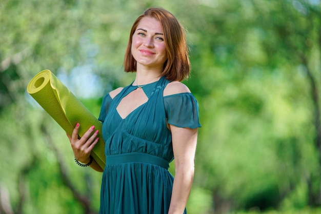 Portret van een jonge vrouw met een sportieve gedraaide mat op een onscherpe achtergrond in het park