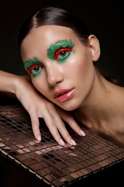 Portret van een jonge vrouw met felrode en groene creatieve make-up op een donkere achtergrond Schoonheidsmode