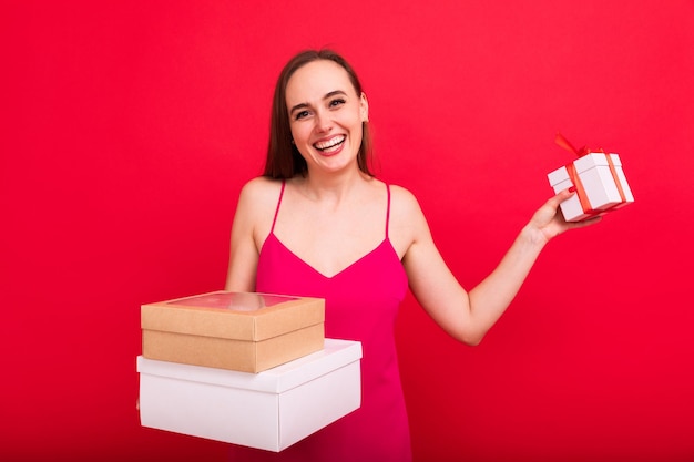 Portret van een jonge vrouw met geschenken in haar handen op een rode achtergrond Kersttraditie van het geven van geschenken