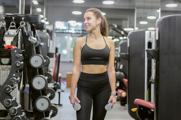 Portret van een jonge vrouw met halters in haar handen in een moderne gymxA