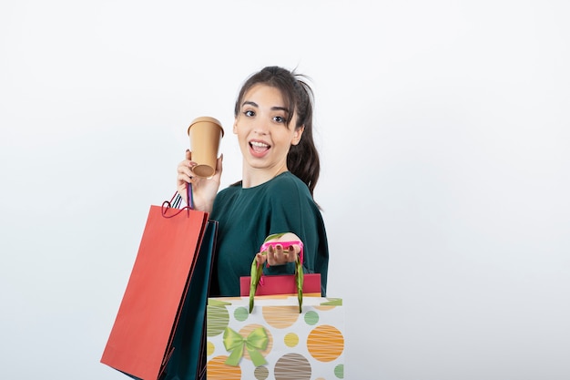 Portret van een jonge vrouw met kleurrijke boodschappentassen met een kopje.