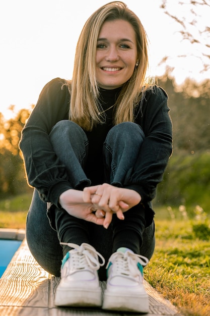 Portret van een jonge vrouw met kort blond haar die lacht voor de camera op de grond zit