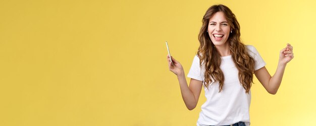 Portret van een jonge vrouw met opgeheven armen die tegen een gele achtergrond staat