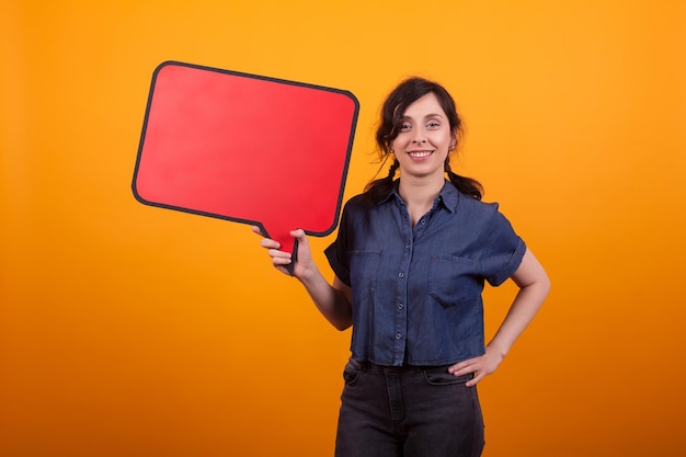 Portret van een jonge vrouw met rode gedachte bel over gele achtergrond in de studio. Vrolijke vrouw met banner in haar hand.