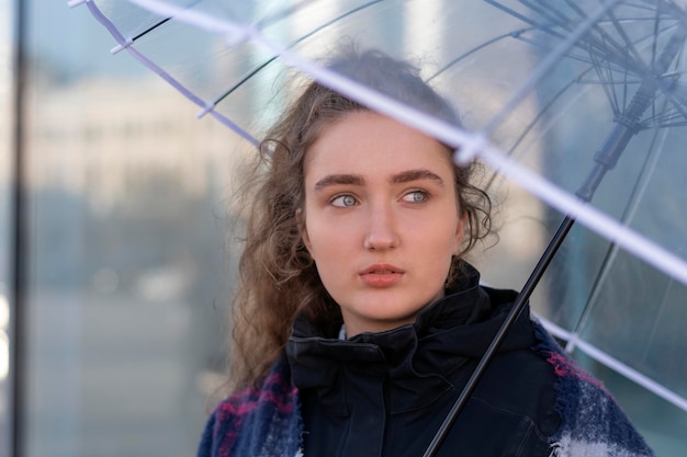 Portret van een jonge vrouw met weelderig lang bruin haar onder transparante paraplu Kijk aan de zijkant Verticaal frame