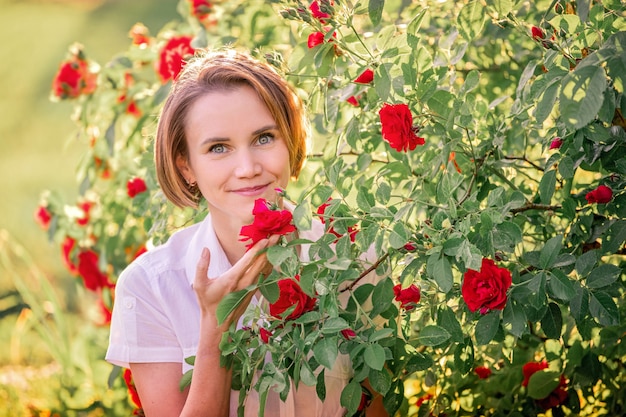 Portret van een jonge vrouw onder rode rozen in het achterzonlicht
