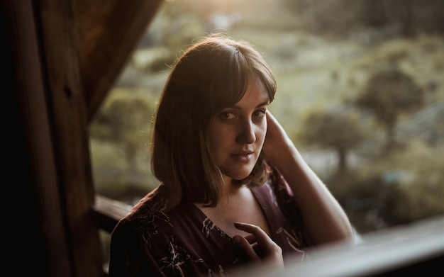 Portret van een jonge vrouw op de richel van een houten hut bij zonsondergang