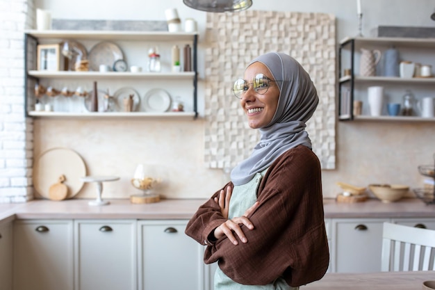 Portret van een jonge vrouw van oosterse afkomst in een hijab en een schort die thuis in de keuken staat