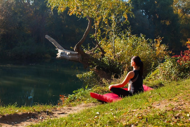 Portret van een jonge vrouw zittend op roze yogamat in het zomerbos en mediteren met gesloten ogen in het zonlicht. Gezond levensstijlconcept