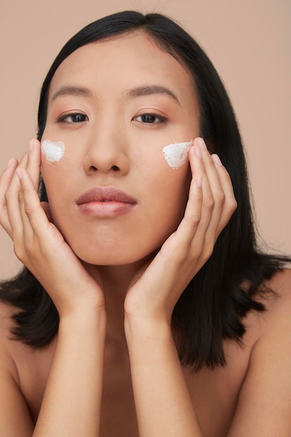 Portret van een jonge vrouwelijke Chinese vrouw die crème aanbrengt