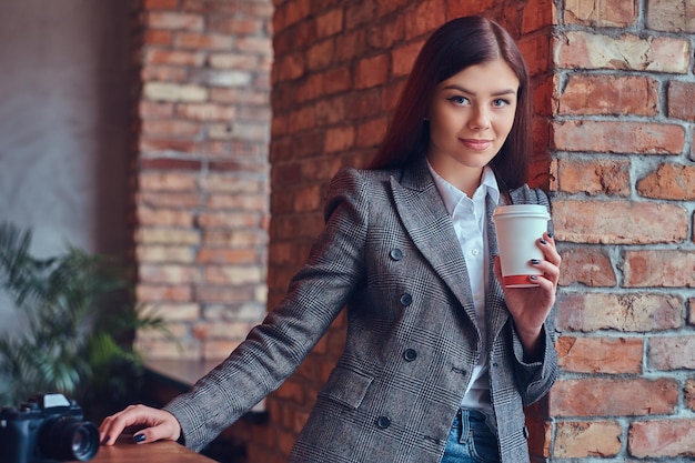 Portret van een jonge vrouwelijke fotograaf houdt een kopje 's ochtends vast