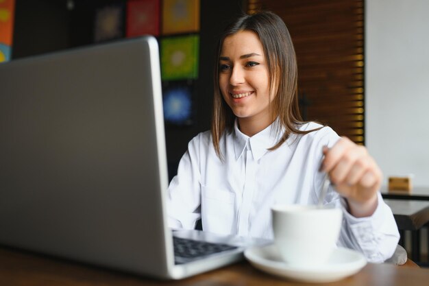 Portret van een jonge vrouwelijke freelancer die een laptopcomputer gebruikt voor een baan op afstand terwijl hij in het interieur van een moderne coffeeshop zit, slimme blonde vrouw die aan het boek werkt tijdens het ochtendontbijt in de café-bar