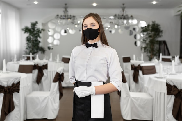 Portret van een jonge vrouwelijke ober met een beschermend medisch masker tijdens quarantaine Covid19