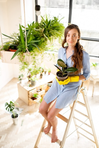 Portret van een jonge vrouwelijke tuinman met een bloempot op de ladder in de oranjerie