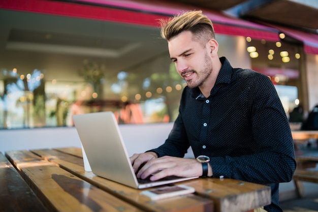 Portret van een jonge zakenman die op zijn laptop werkt terwijl hij in een coffeeshop zit