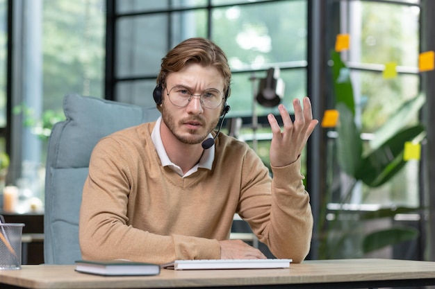 Portret van een jonge zakenman man in een headset die geconcentreerd werkt vanuit een kantoor aan huis spreekt