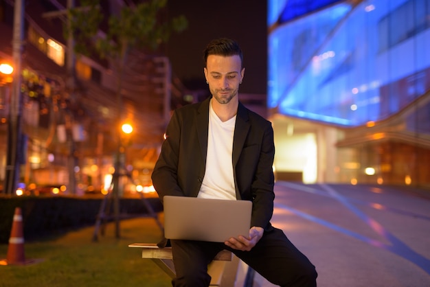 Portret van een jonge zakenman met laptop tegen een 's nachts stad