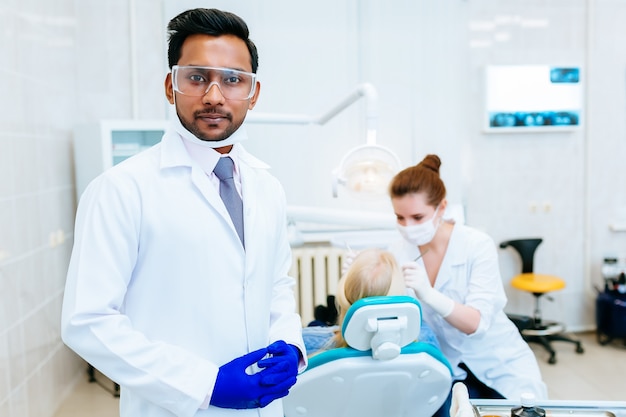 Portret van een jonge zekere Aziatische mannelijke tandarts in kliniek voor vrouwelijke tandarts die tanden controleren aan patiënt. Tandheelkundige kliniek concept