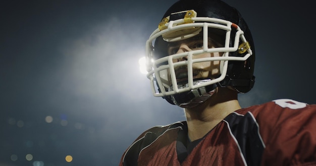 portret van een jonge zelfverzekerde American football-speler die 's nachts op het veld staat