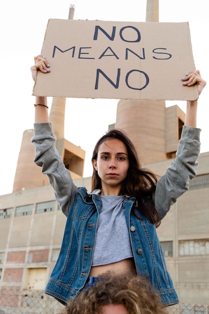 Portret van een jonge zelfverzekerde vrouw met een nee betekent geen banner in een demonstratie voor empowerment van vrouwen. Zittend op de schouder van de man. Gelijkheid concept.