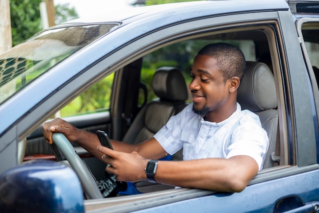 Portret van een jonge zwarte Afrikaanse knappe chauffeur in taxi-auto met behulp van slimme telefoontechnologie