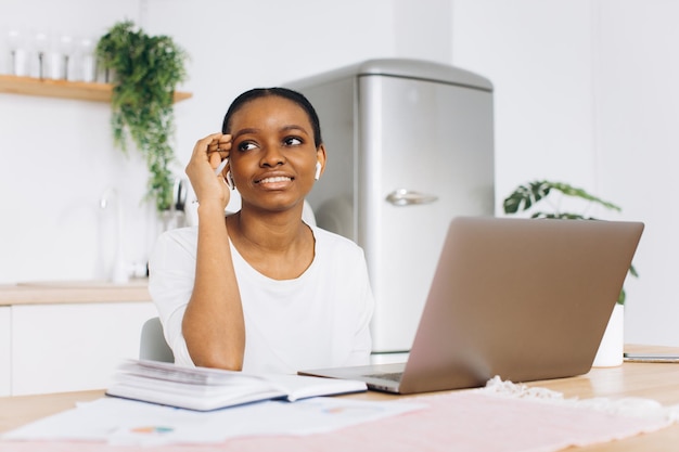 Portret van een jonge zwarte vrouw die in de keuken zit en thuis op een laptop werkt.