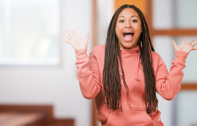 Portret van een jonge zwarte vrouw met vlechten schreeuwen blij, verrast door een aanbod of een promotie