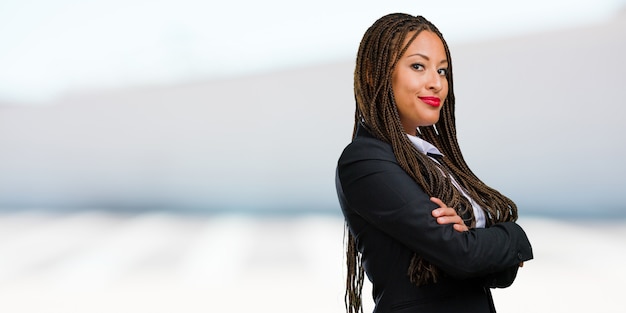 Portret van een jonge zwarte zakenvrouw overschrijding van zijn armen, glimlachend en blij, zelfverzekerd en vriendelijk