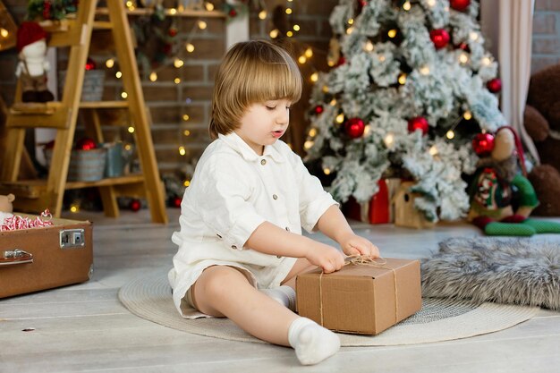 Portret van een jongen bij de kerstboom die een kerstcadeau uitpakt