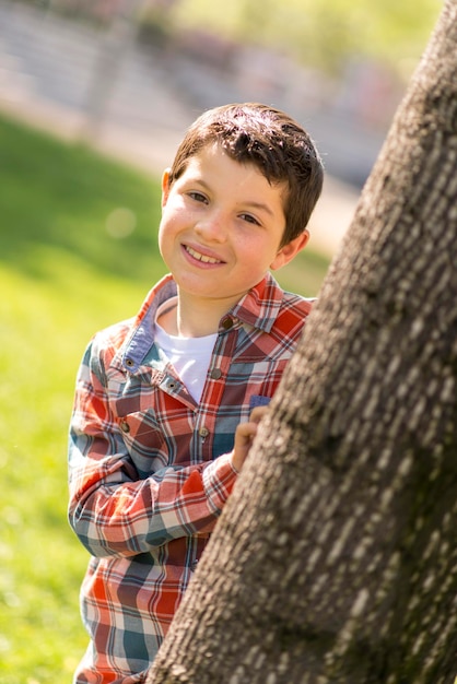 Portret van een jongen die achter een boomstam in het park staat