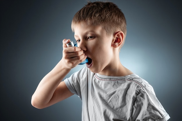 Portret van een jongen die een astma-inhalator gebruikt om ontstekingsziekten, kortademigheid te behandelen. Het concept van behandeling voor hoest, allergieën, aandoeningen van de luchtwegen.