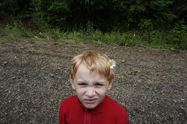 Foto portret van een jongen die een bloem draagt terwijl hij op het veld staat