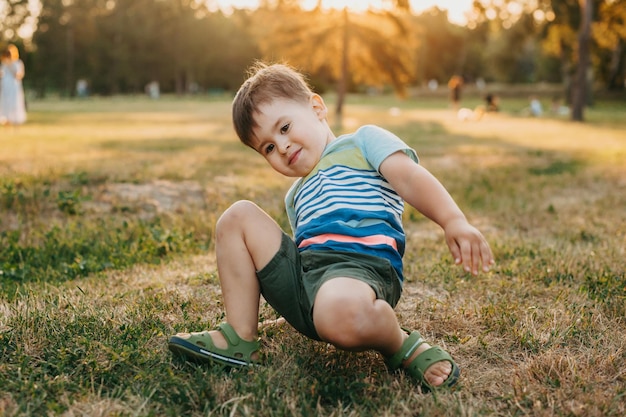 Portret van een jongen die probeert op te staan nadat hij naar beneden is gevallen in het park groene grasveld actieve levensstijl...