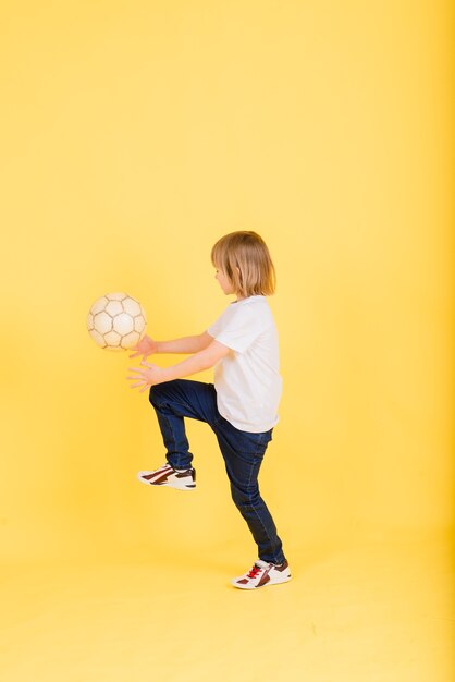 Portret van een jongen die voetbal vasthoudt, studio gele achtergrond