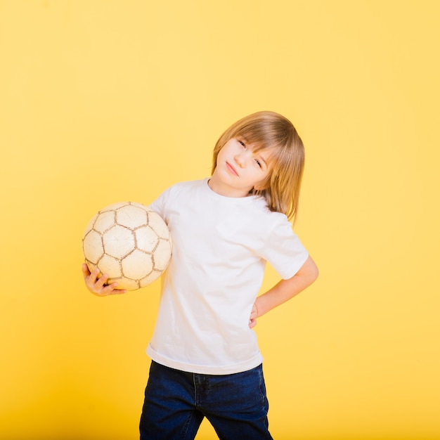 Portret van een jongen die voetbal vasthoudt, studio gele achtergrond