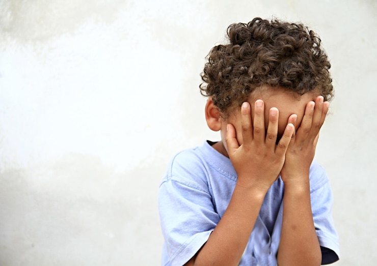 Foto portret van een jongen die zijn gezicht met zijn handen bedekt