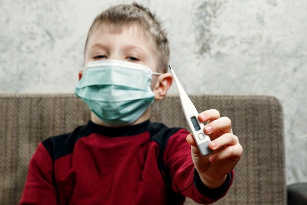 Portret van een jongen, een kind in een medisch masker houdt een thermometer in zijn handen