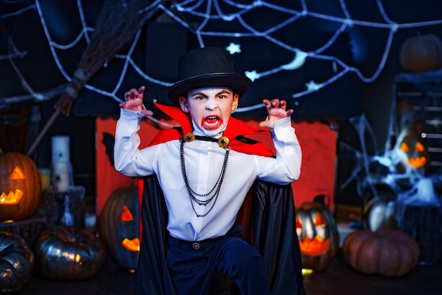 Portret van een jongen gekleed in een kostuum van een vampier en hoed over grungeachtergrond. Halloween feest.