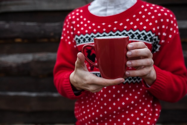 Foto portret van een jongen in een kerstmissweater die koffie drinken, op een achtergrond van houten muur