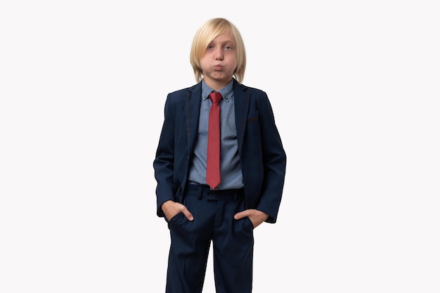 Portret van een jongen in een zakenpak met opgeblazen wangen houdt handen in zakken geïsoleerd op witte achtergrond