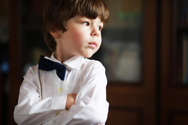 Portret van een jongen met bruine ogen in een overhemd en een zwarte vlinderdas op een donkere achtergrond. het kind is emotioneel, lacht, heeft plezier, is gelukkig.