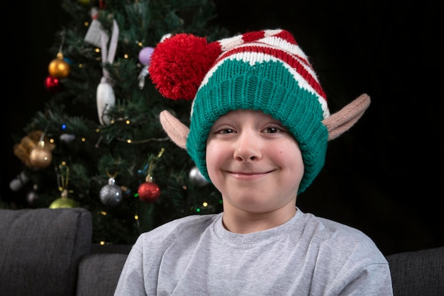 Portret van een jongen met een kerstelf-hoed tegen de achtergrond van de kerstboom