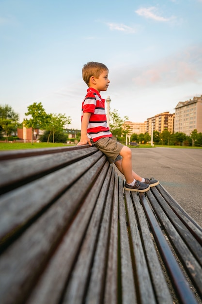 Portret van een jongen met een korte broek die op een houten bankpark zit te ontspannen op een verveelde zomerdag