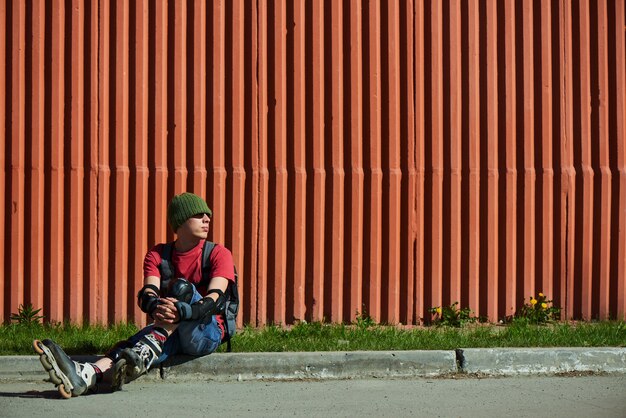 Portret van een jongen op rolschaatsen die op de stoep tegen de rode muur zit