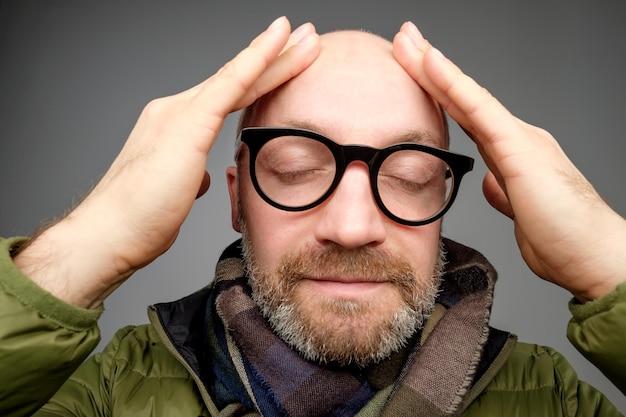 Portret van een kale volwassen man met een baard die met zijn vingers over zijn hoofd strijkt hij is kalm en tevreden