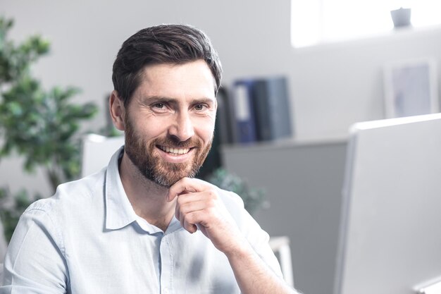 Portret van een kantoormedewerker Hij kijkt naar de camera en glimlacht Zittend aan een bureau op kantoor achter de computer in een wit overhemd
